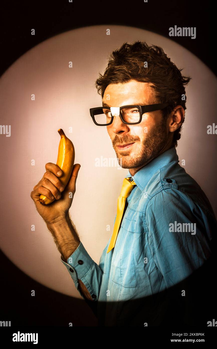 Giovane imprenditore dorky tenendo una banana pistola sul cerchio parete office. Chiamata all'azione Foto Stock