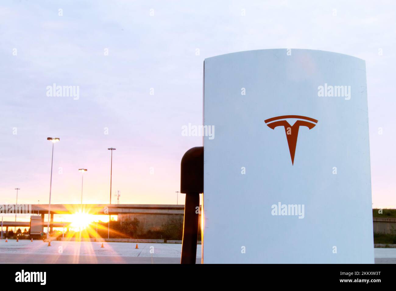 Un logo rosso Tesla sulla parte anteriore di un Supercharger Tesla è visto come l'alba splende sullo sfondo. Foto Stock