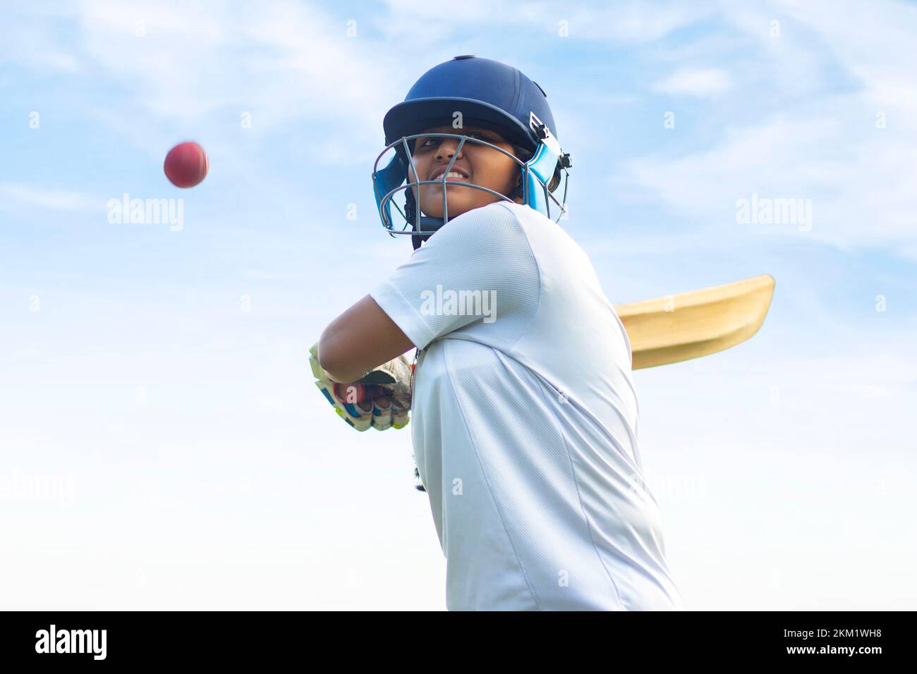 Giocatore di cricket femminile che indossa un equipaggiamento protettivo e colpisce il pallone con un pipistrello sul campo Foto Stock