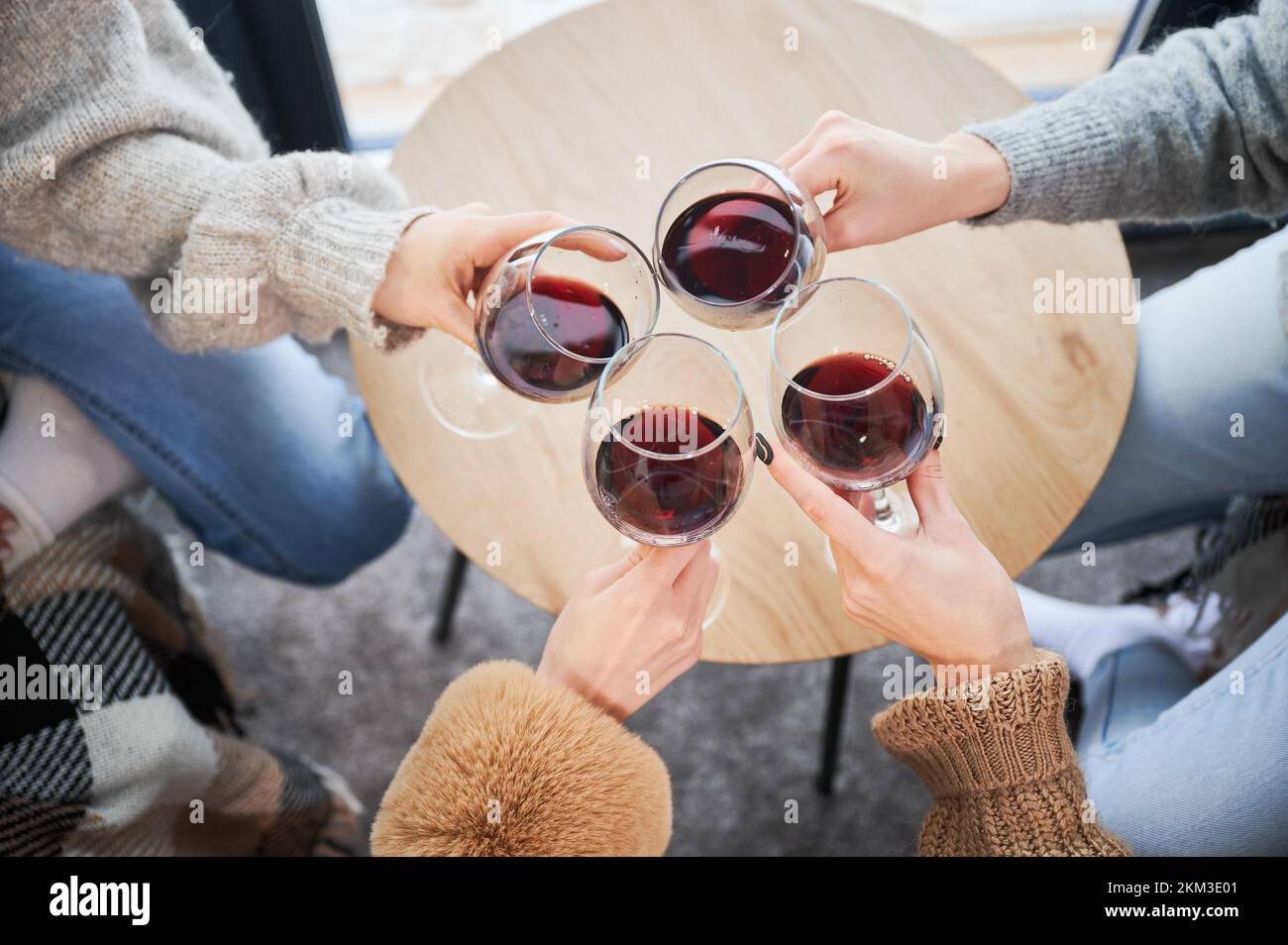 Vista ritagliata delle giovani donne che indossano bicchieri e bevono vino rosso. Le ragazze che si godono i fine settimana invernali all'interno di una casa fienile contemporanea. Foto Stock