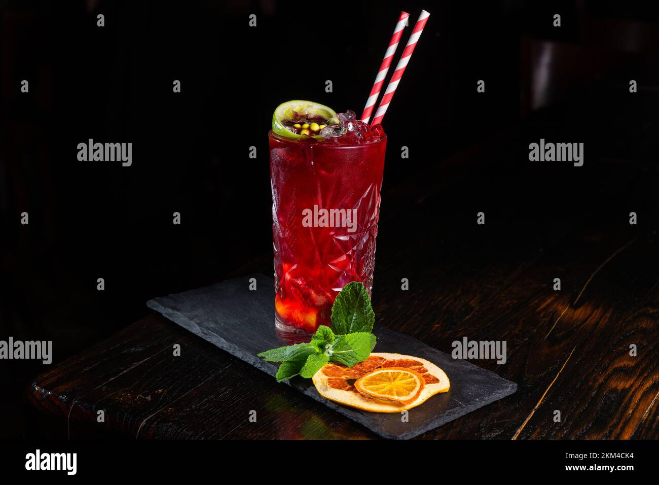 Basso angolo primo piano di gourmet antico cocktail artigianale di rum e bevande gassate guarnito da calce, arancia secca e menta sul bar tenere con backgro scuro Foto Stock