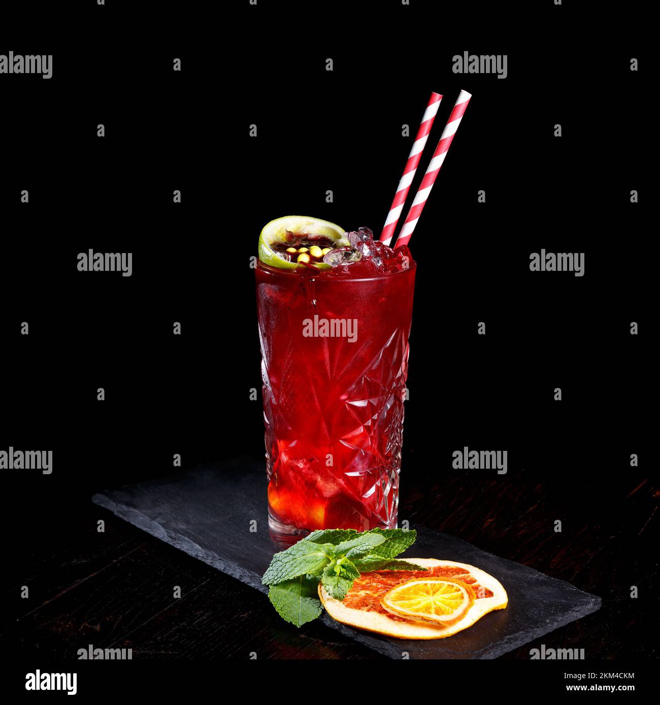 Basso angolo primo piano di gourmet antico cocktail artigianale di rum e bevande gassate guarnito da calce, arancia secca e menta sul bar tenere con backgro scuro Foto Stock