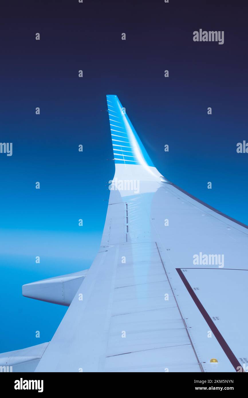 Guardando fuori la finestra dell'aeroplano e vedendo la punta dell'alare riflessa sull'ala dell'aereo. Con uno sfondo blu intenso. Foto Stock
