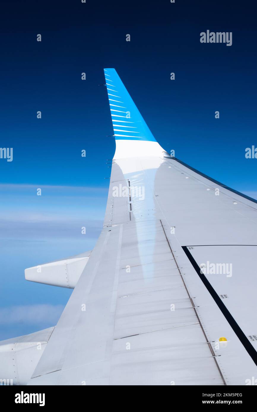 Guardando fuori la finestra dell'aeroplano e vedendo la punta dell'alare riflessa sull'ala dell'aereo. Con uno sfondo blu intenso. Foto Stock