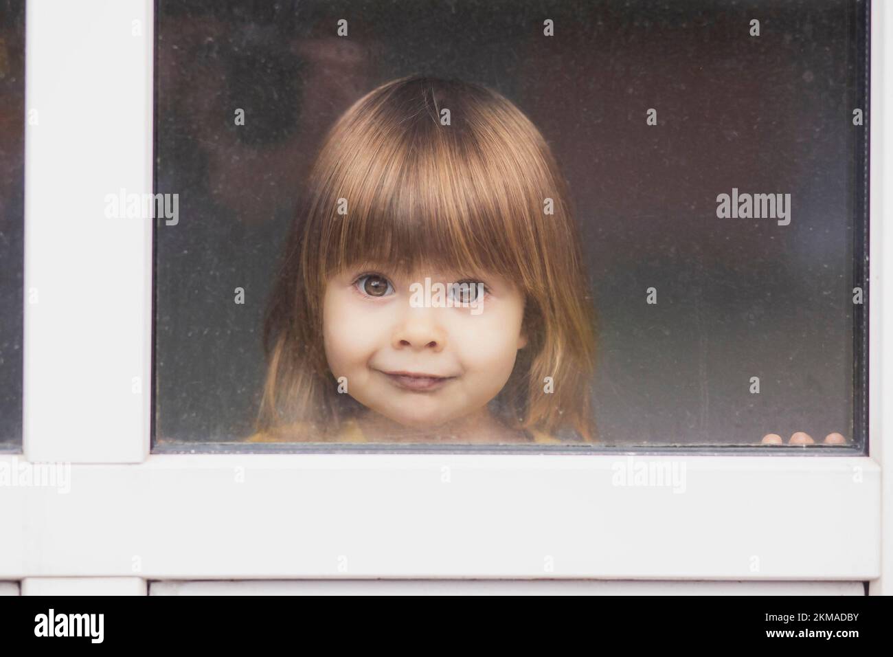 Bello bambino con capelli leali che guarda fuori dalla finestra Foto Stock