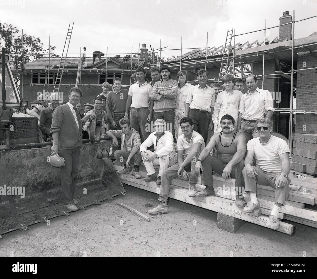 1980s, storico, fuori su un cantiere di nuove case, il team di lavoratori si riuniscono accanto a un digger per una foto di gruppo, Inghilterra, Regno Unito. Foto Stock
