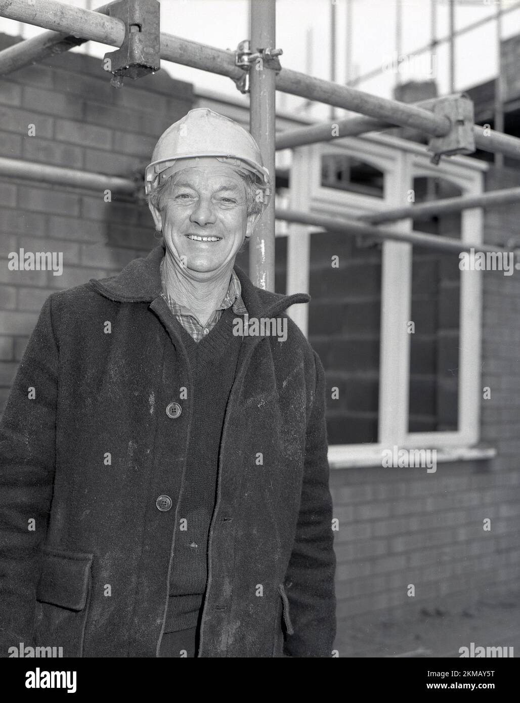 1980s, storico, costruttore in giacca doney in piedi per la sua foto all'esterno su un cantiere, nuove case in costruzione, Inghilterra, Regno Unito. Foto Stock