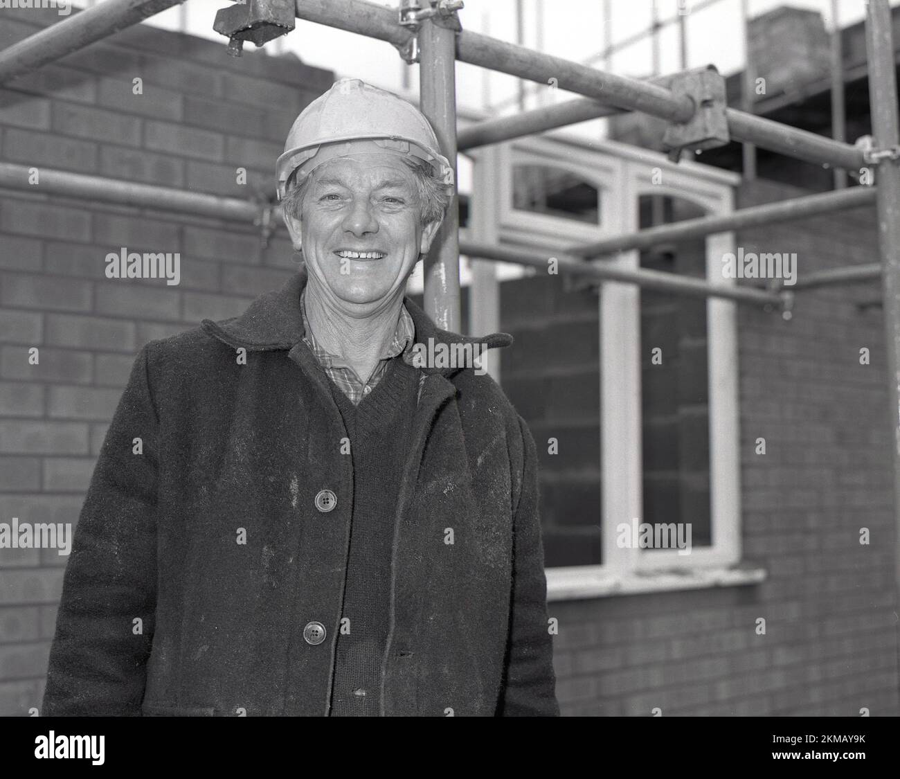 1980s, storico, costruttore in giacca doney in piedi per la sua foto all'esterno su un cantiere, nuove case in costruzione, Inghilterra, Regno Unito. Foto Stock