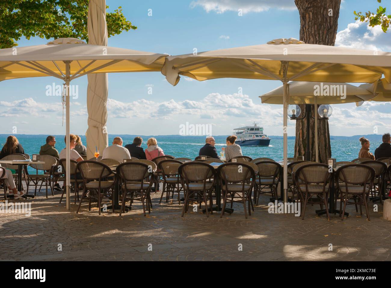 Lago di Garda, vista delle persone che si rilassano ai tavoli da caffè posti lungo il lungomare nella panoramica zona del centro storico di Garda, Lago di Garda, Veneto Foto Stock