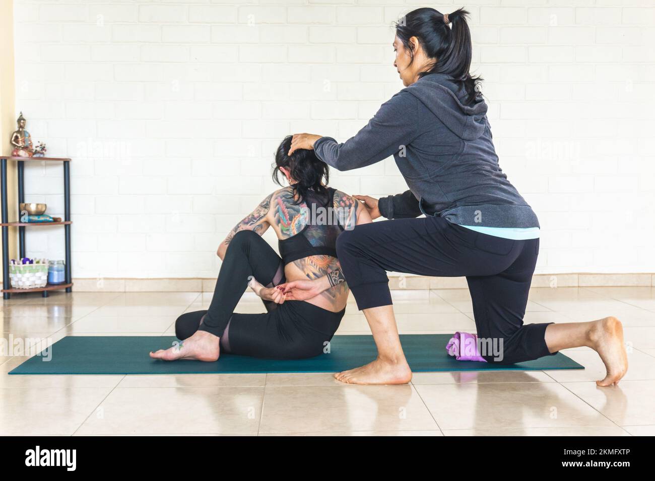 Istruttore di yoga che corregge la postura di uno studente che fa ardha matsyendrasana Foto Stock