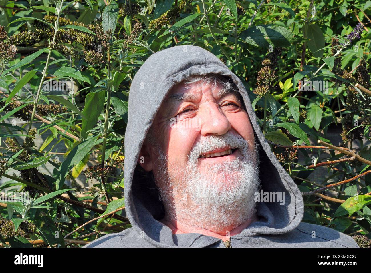 Uomo felice vecchio o anziano che indossa un cappuccio e che sorride verso la fotocamera. Foto Stock