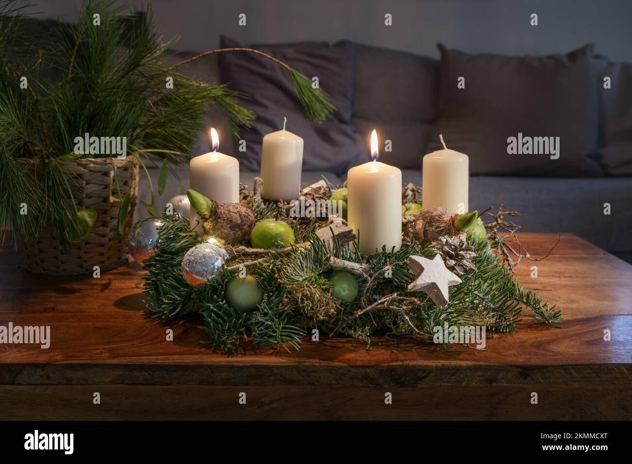 Secondo Avvento, corona con due candele bianche brucianti e decorazione di Natale su un tavolo di legno di fronte al divano, decorazione casa di festa, spazio copia, Foto Stock