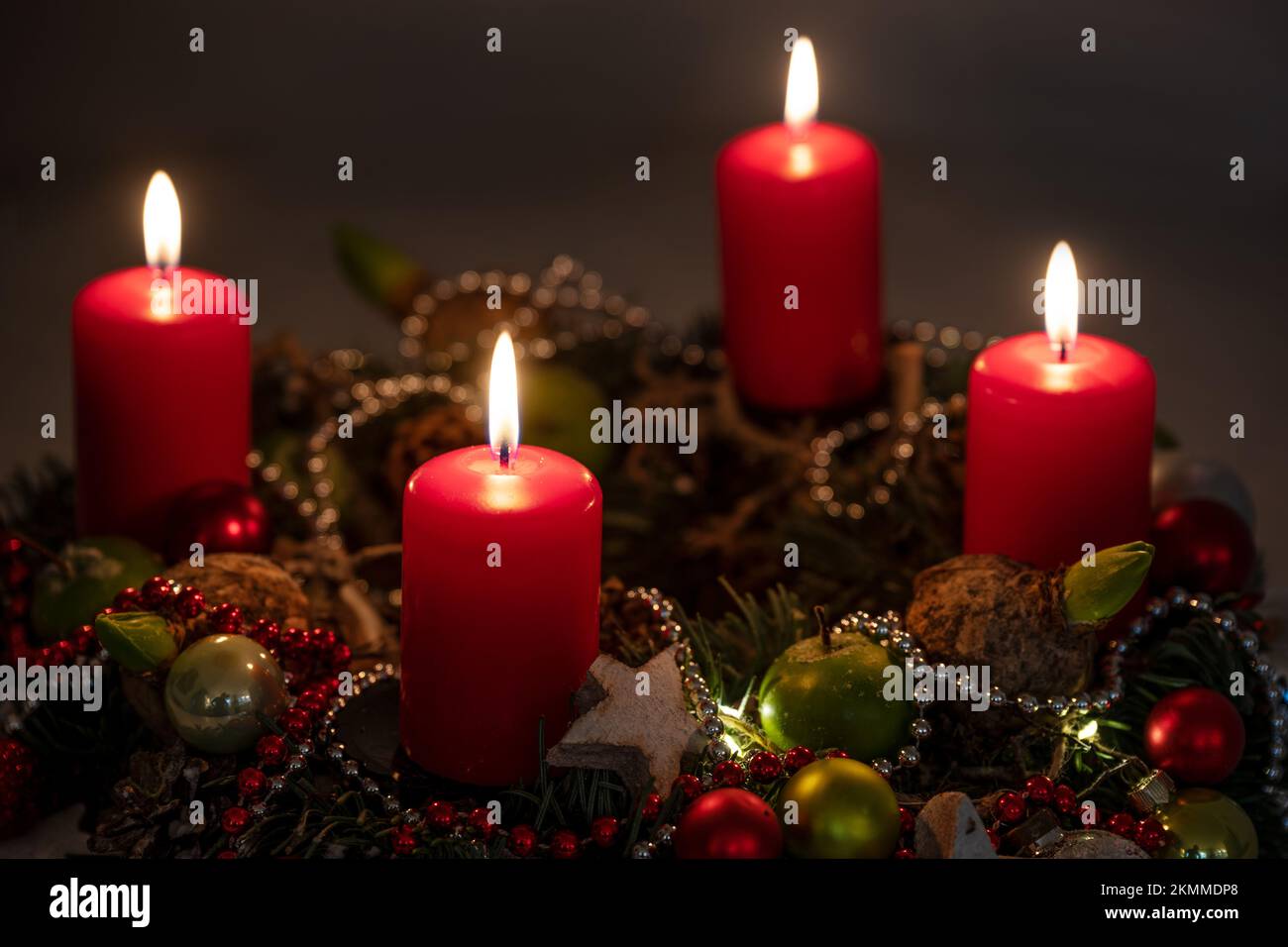 Luci di Avvento e Natale, quattro candele rosse su una corona con decorazione su uno sfondo scuro, spazio copia, messa a fuoco selezionata, profondità di campo stretta Foto Stock