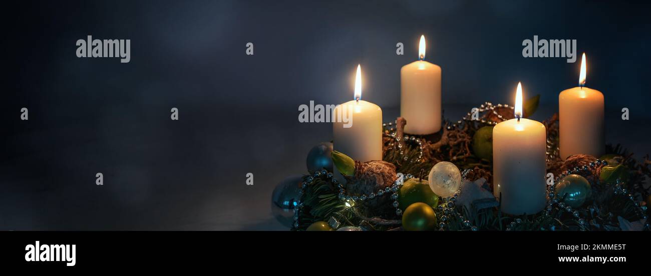 Luci di notte, quattro candele di Avvento bianche su una corona con decorazione di Natale su uno sfondo blu scuro, formato panoramico, spazio copia, sel Foto Stock
