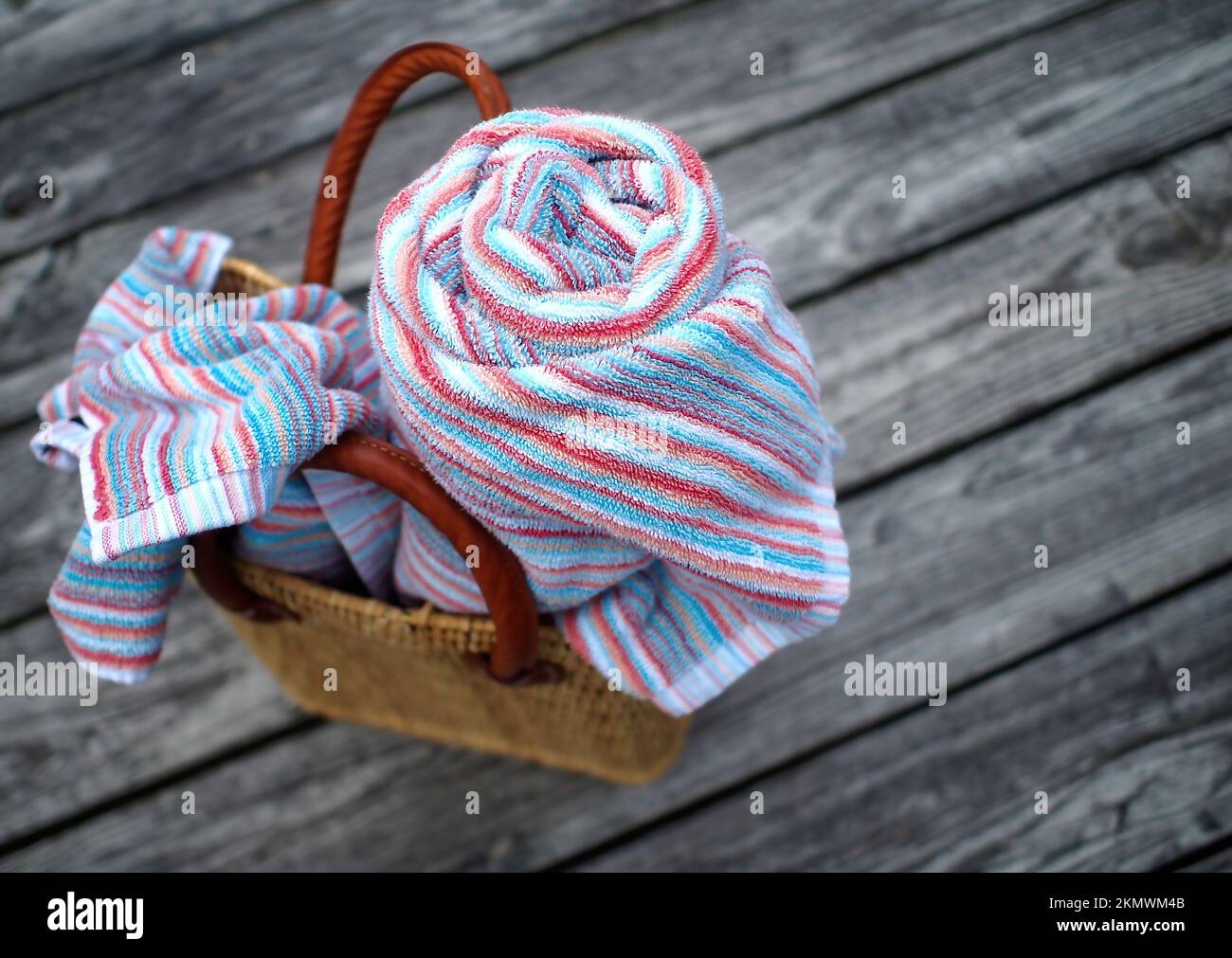 Per una giornata in spiaggia - tote da spiaggia in tessuto con fasce in pelle; con teli da spiaggia colorati, uno arrotolato, uno sciolto, su ruvido, rustico, weathe Foto Stock