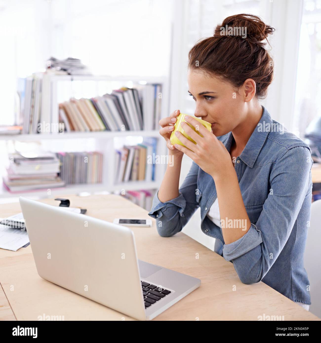 Inizia la giornata di lavoro con un po' di caffè fresco. una donna attraente che usa il suo notebook a casa. Foto Stock
