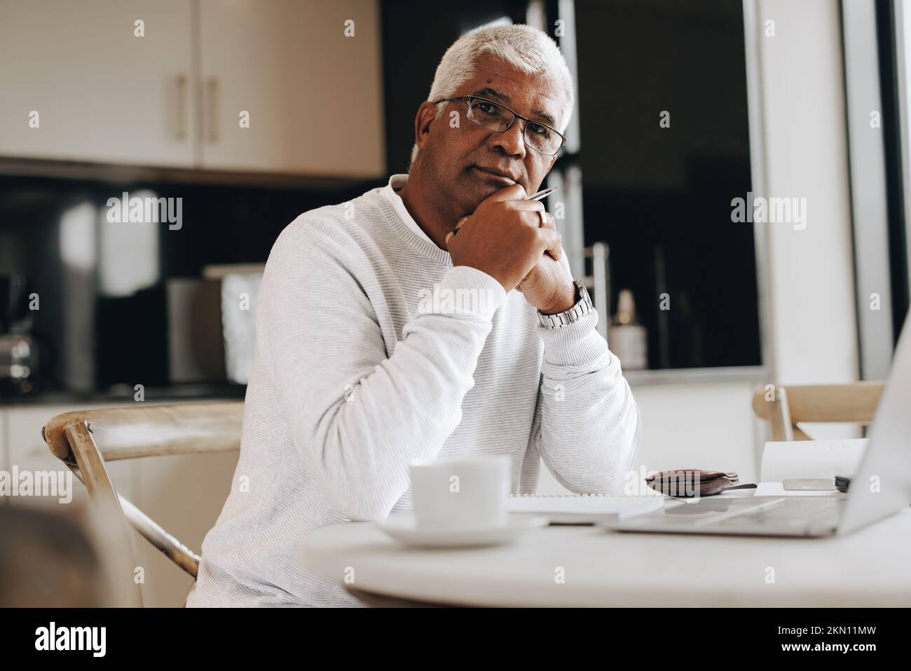 Professionista maturo che guarda la fotocamera mentre si siede alla scrivania di casa. Uomo d'affari senior che utilizza un computer portatile mentre lavora da casa. Foto Stock