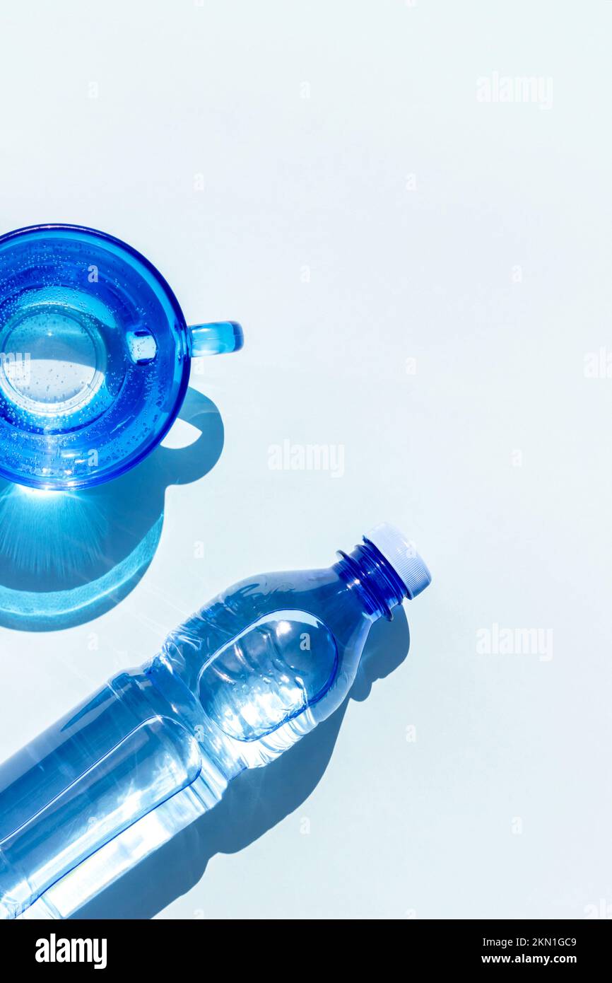 Acqua in bottiglia. Una bottiglia di acqua minerale e un bicchiere d'acqua con ombre dure su sfondo blu. Piano Lay Vista superiore Copia spazio. Foto Stock