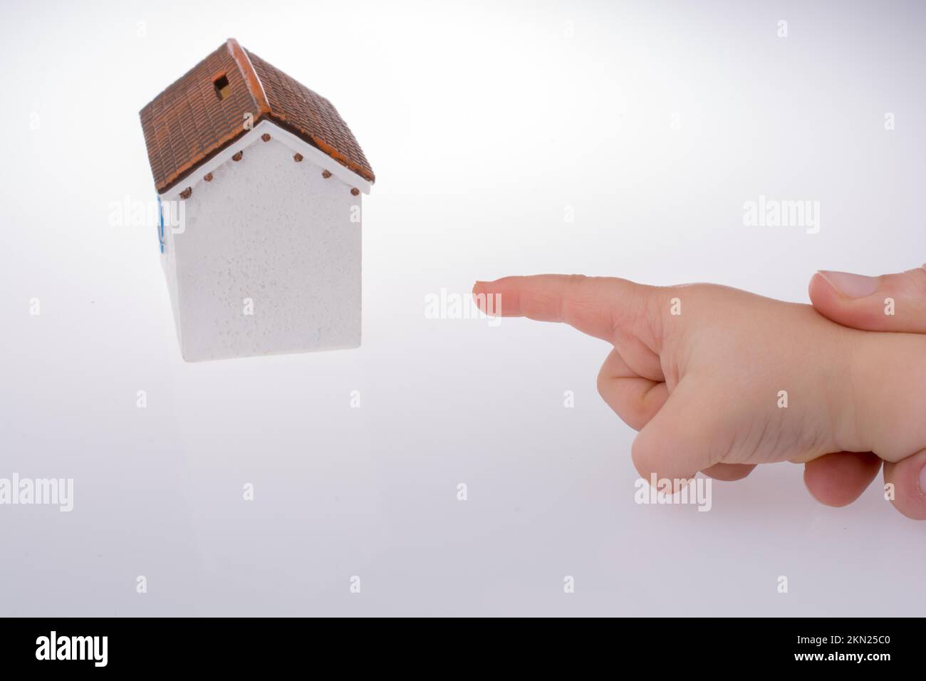 Piccola mano che indica una casa modello su uno sfondo di colore bianco Foto Stock
