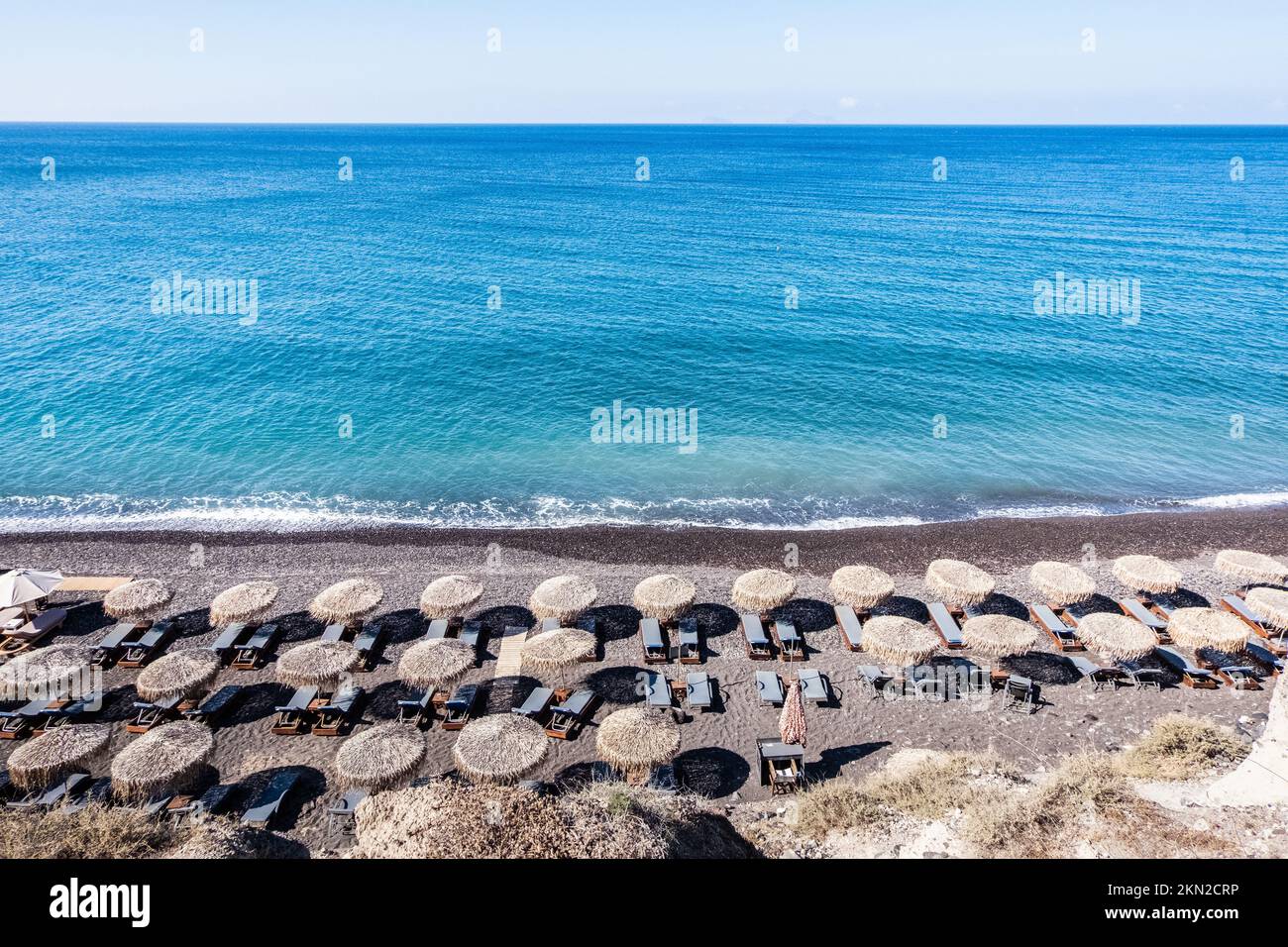 Splendida vista sul mare dell'isola di Santorini da una collina con lettini e ombrelloni sulla spiaggia Foto Stock