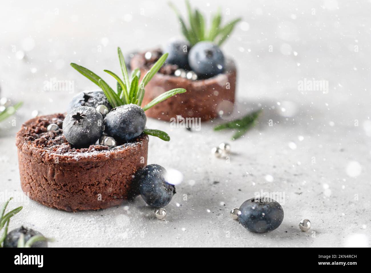 Brownie al cioccolato decorate con mirtilli e rosmarino su sfondo bianco testurizzato con luci bokeh. Natale, Capodanno ricetta concetto. Chiudi Foto Stock
