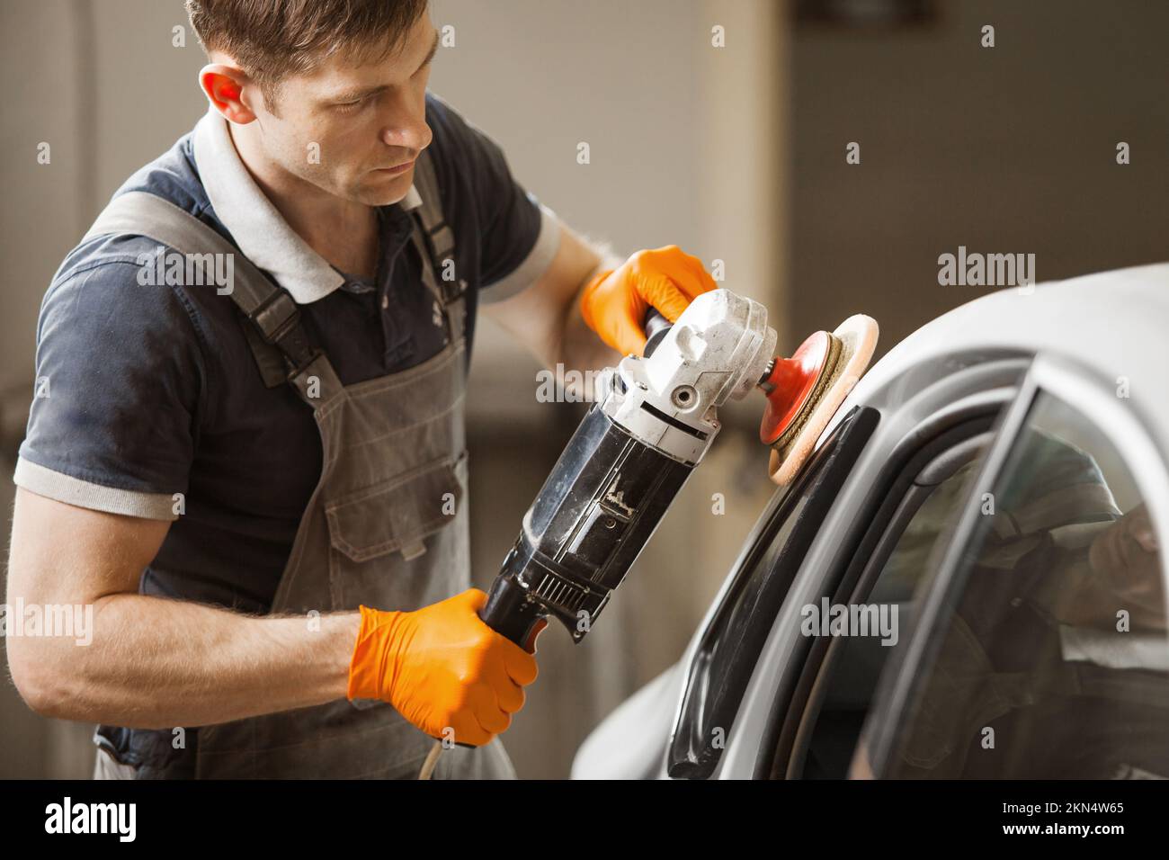 Dettaglio auto - l'operaio maschile tiene una lucidatrice in mano e lucida l'auto bianca in negozio di riparazione auto. Foto Stock