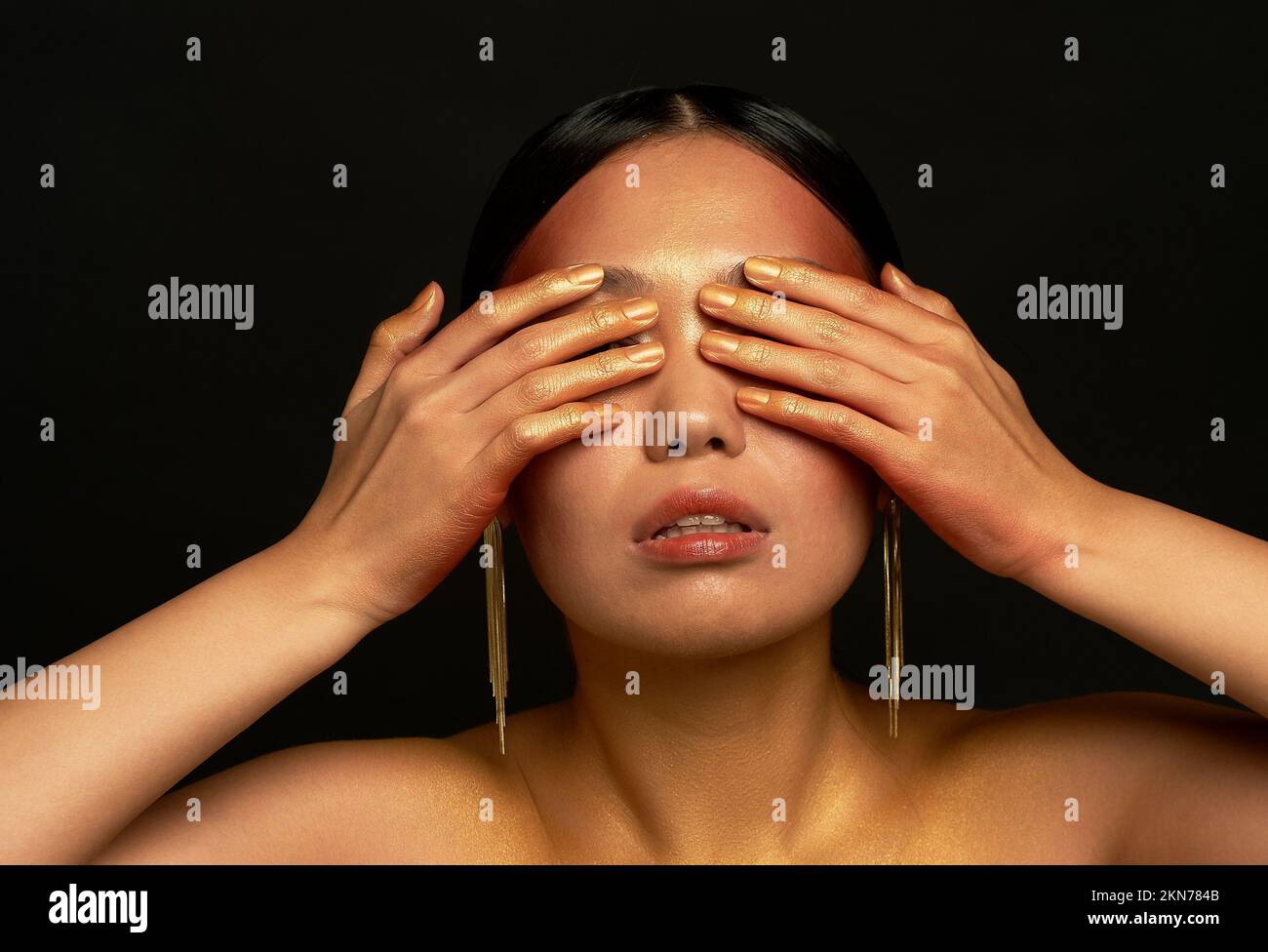 Non vedo il male. Una ragazza asiatica su sfondo nero in uno studio fotografico. Oro. Foto Stock