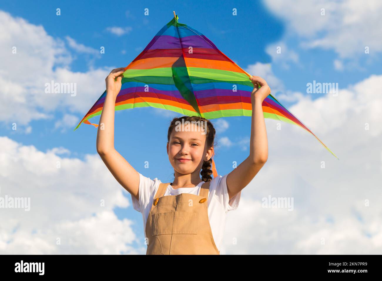 la ragazza tiene un aquilone luminoso sopra la sua testa contro il cielo blu. Foto Stock