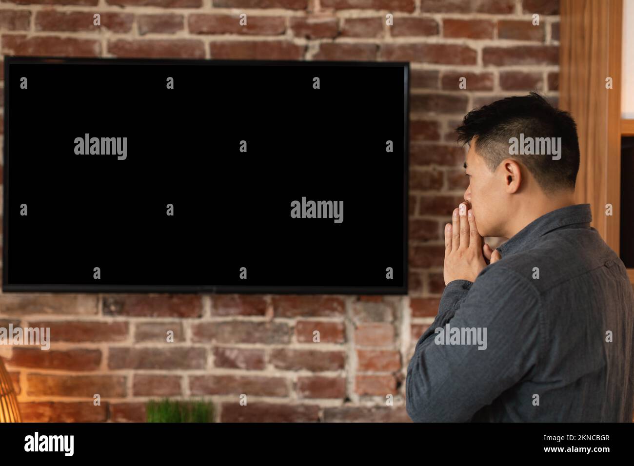 Triste preoccupato asiatico di mezza età maschio guardare le notizie sulla grande tv con schermo vuoto in casa ufficio interno, profilo Foto Stock