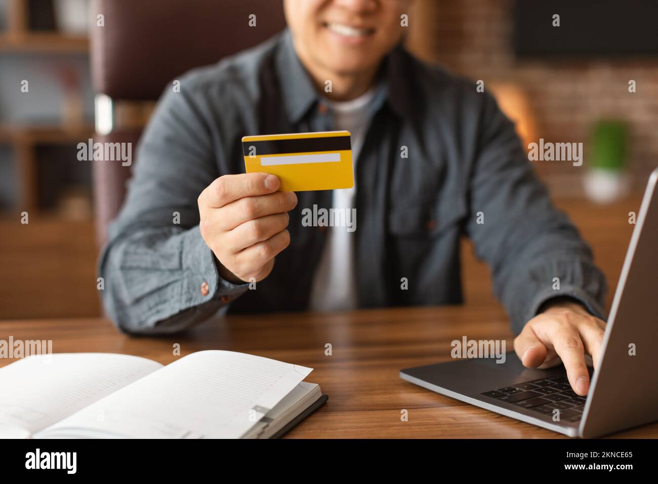 Allegro uomo asiatico adulto utilizzare la carta di credito, digitando sul computer, godere di investimenti e lo shopping online a casa Foto Stock