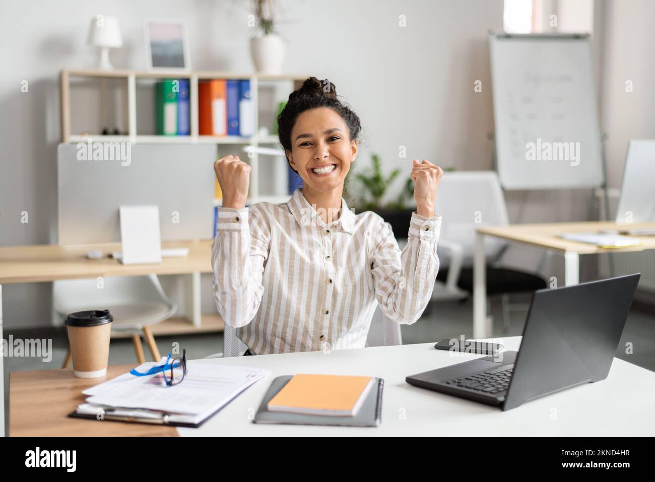 Fortuna per il business. Un'imprenditrice femminile molto gioita che usa il laptop e che scuote i pugni di gioia, festeggia grandi notizie, seduto in ufficio Foto Stock