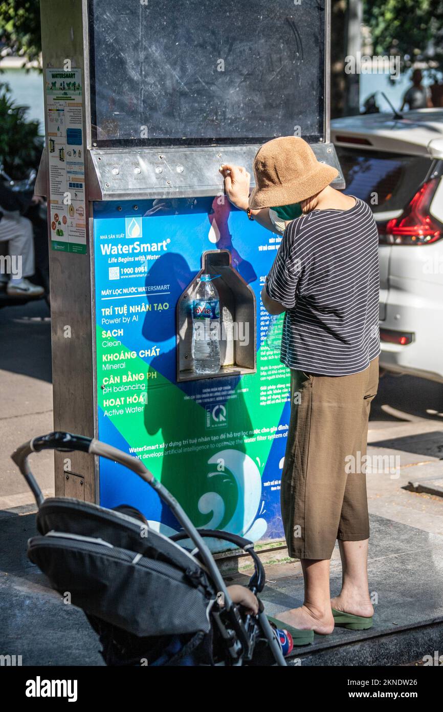 Donna che riempie una bottiglia di plastica con acqua potabile filtrata libera, Hanoi, Vietnam Foto Stock