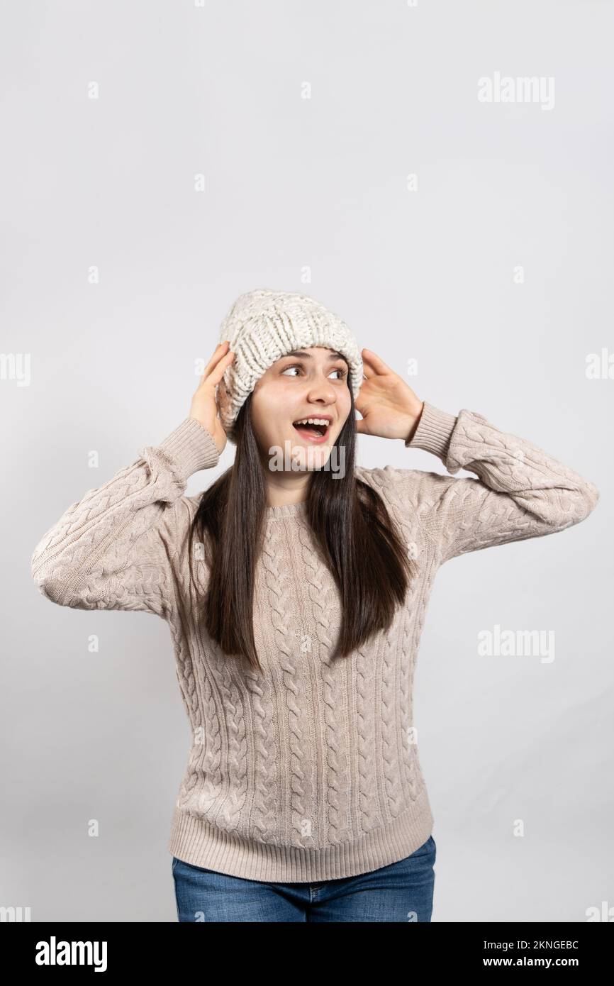 Una donna in un cappello invernale e maglione tiene le mani sulla testa e urla guardando lontano. Foto Stock