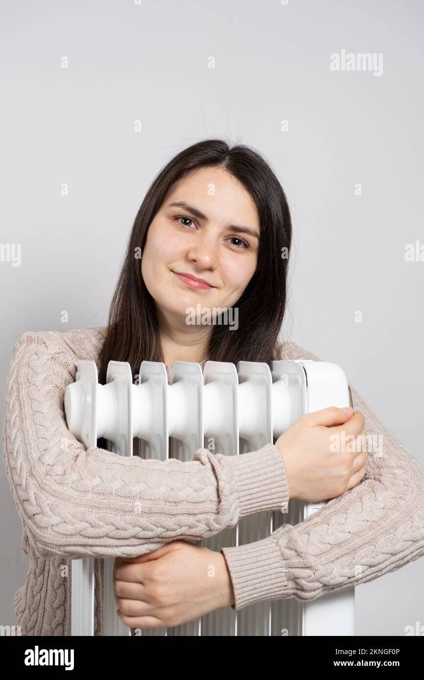 Una donna brunetta abbraccia un riscaldatore elettrico dell'olio, si riscalda in inverno. Foto Stock