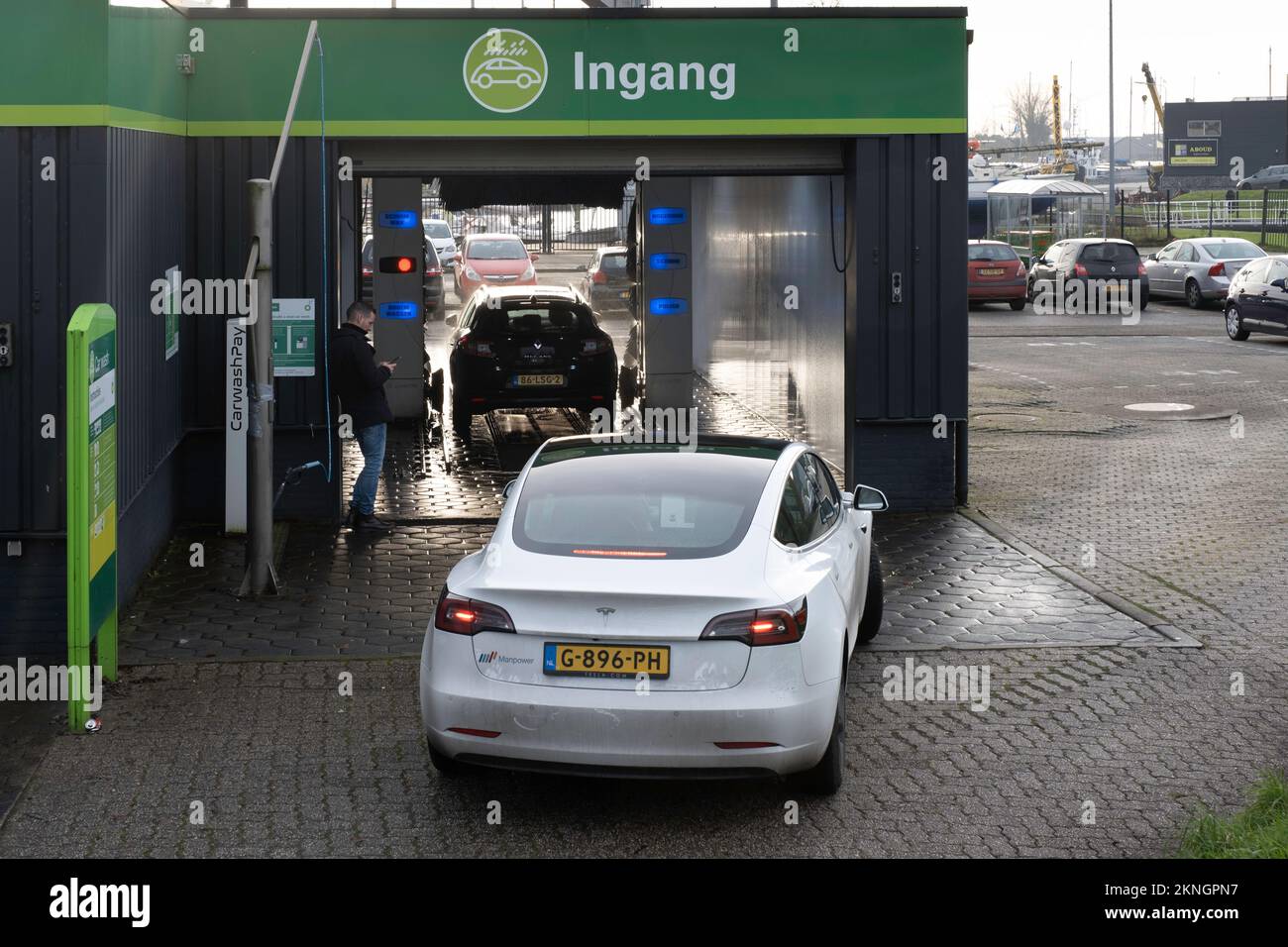Autolavaggio automatico coperto. Un'auto viene lavata, il proprietario sta aspettando all'esterno, una Tesla sta aspettando dietro di essa Foto Stock