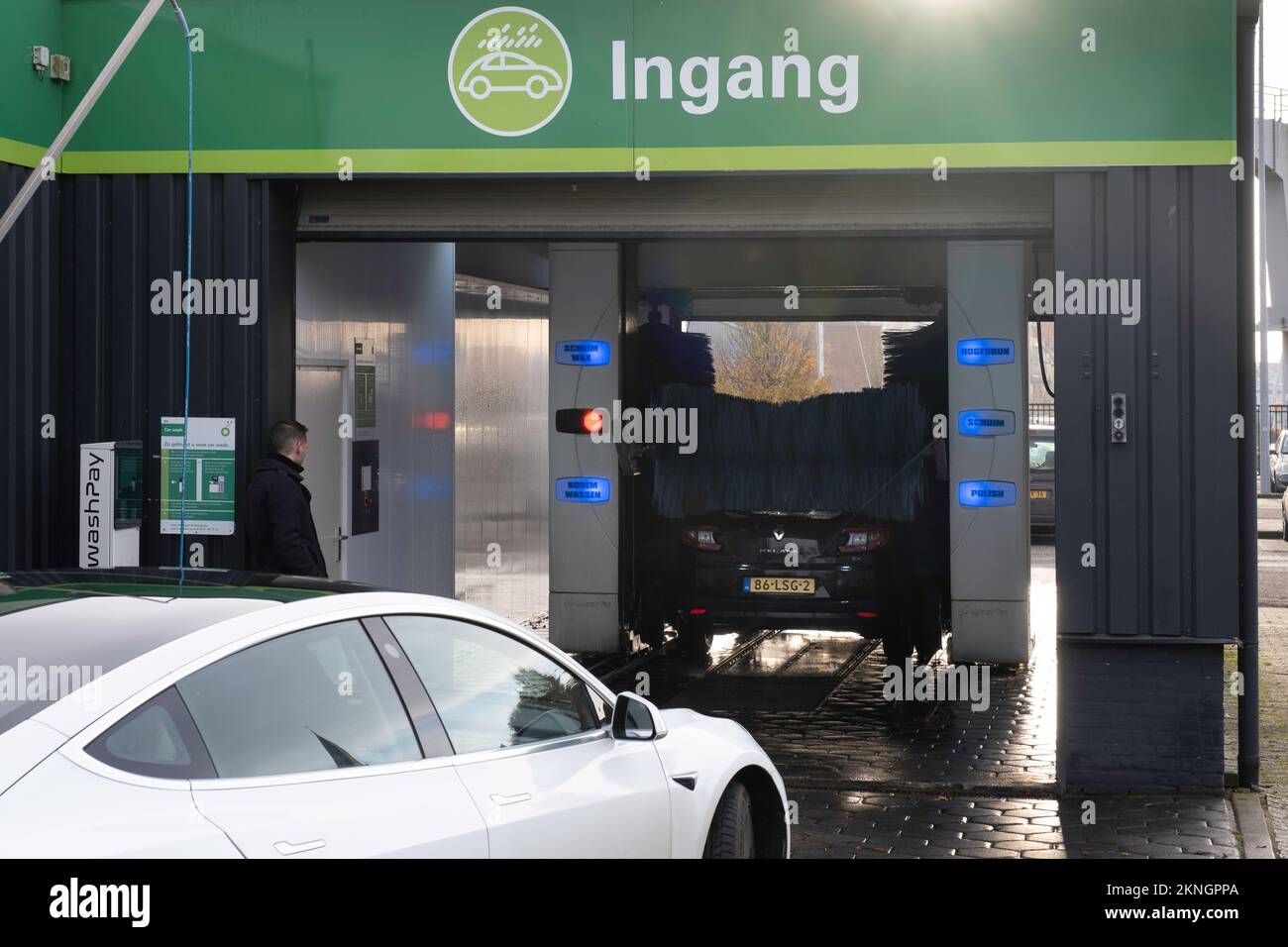 Autolavaggio automatico coperto. Un'auto viene lavata, il proprietario sta aspettando all'esterno, una Tesla sta aspettando dietro di essa Foto Stock