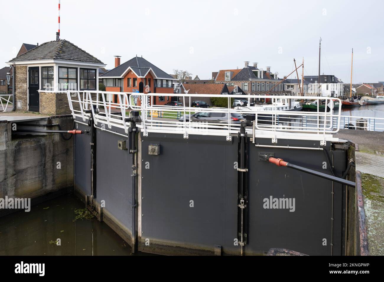 Chiudere i cancelli e chiudere a chiave la casa del guardiano al Riensluis di Lemmer. Sullo sfondo il Polderdijk con case e un hotel e barche sul fiume Rien Foto Stock