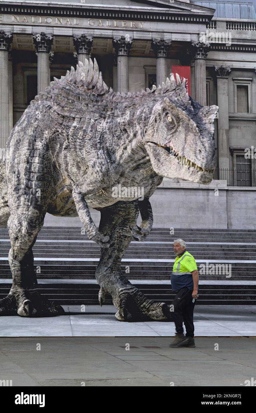 Un operaio che cammina di fronte A Un grande schermo con Un'immagine proiettata di Un T-Rex fuori dalla National Gallery, Londra UK Foto Stock