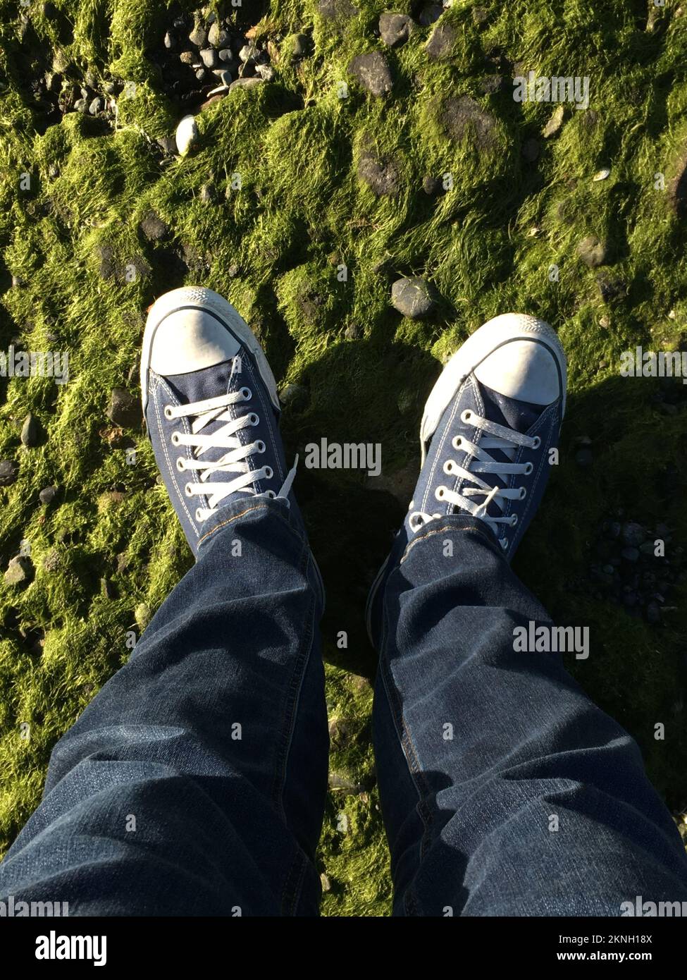 Persona in jeans e scarpe Converse seduta gambe incrociate al di fuori come una seconda persona cammina passato Foto stock Alamy