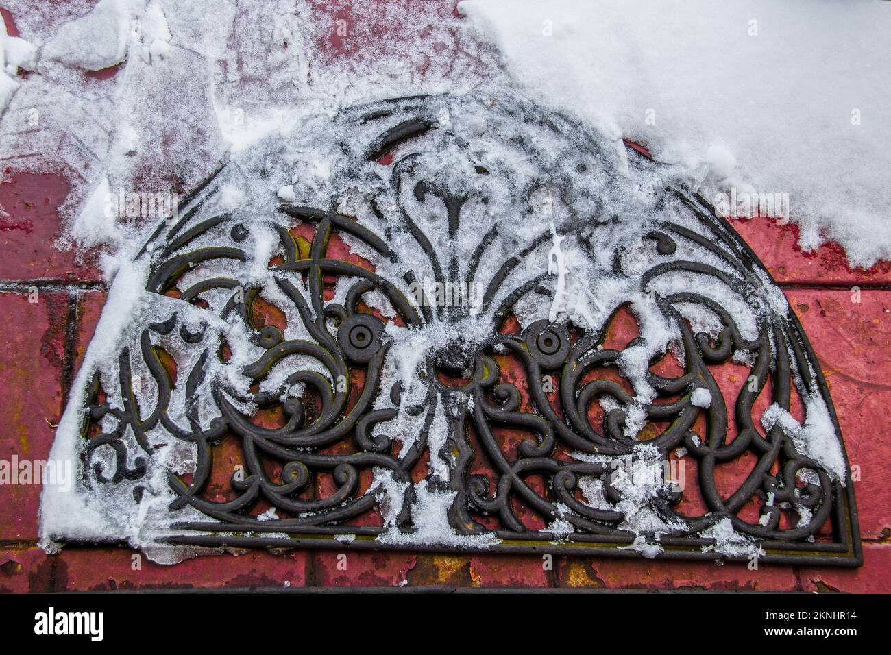 Tappetino porta di benvenuto in gomma ornato in neve con stampe di ghiaccio e scarpe su una superficie esterna in mattoni rossi grungy verniciata - vista dall'alto in basso - primo piano Foto Stock