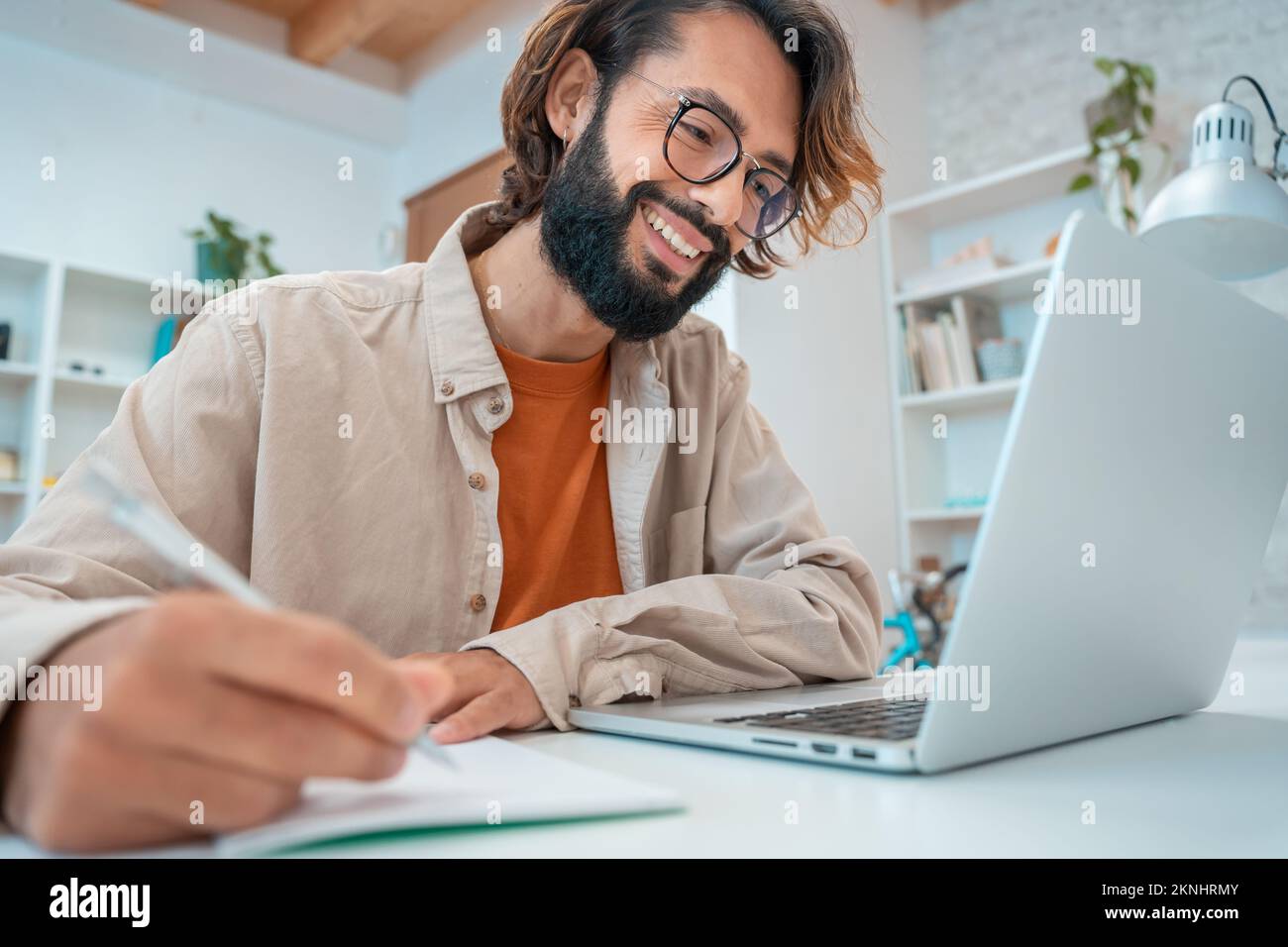 Felice giovane imprenditore creativo ridendo sorridente scrive in un notebook accanto al notebook nel suo ufficio Foto Stock