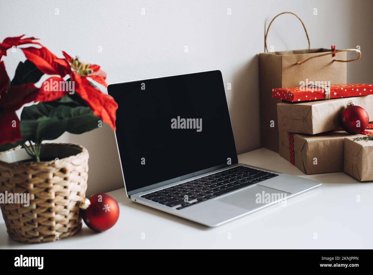 Computer portatile con schermo vuoto e poinsettias Christmas Flower e scatole regalo su un tavolo bianco. Area di lavoro della scrivania dell'ufficio domestico con copia Mock up Foto Stock