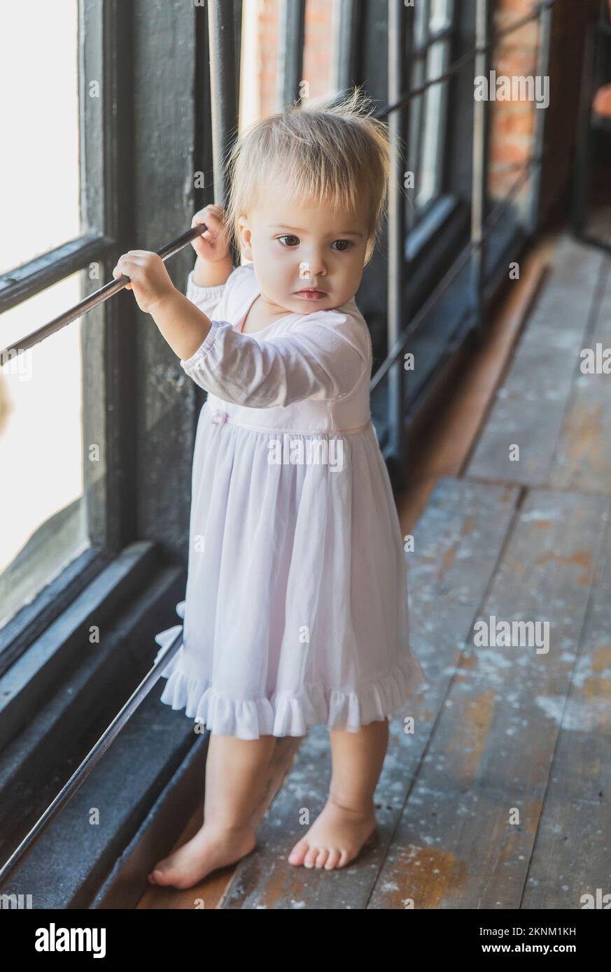 bellissimo bambino biondo in una nightgown vicino alla finestra Foto Stock