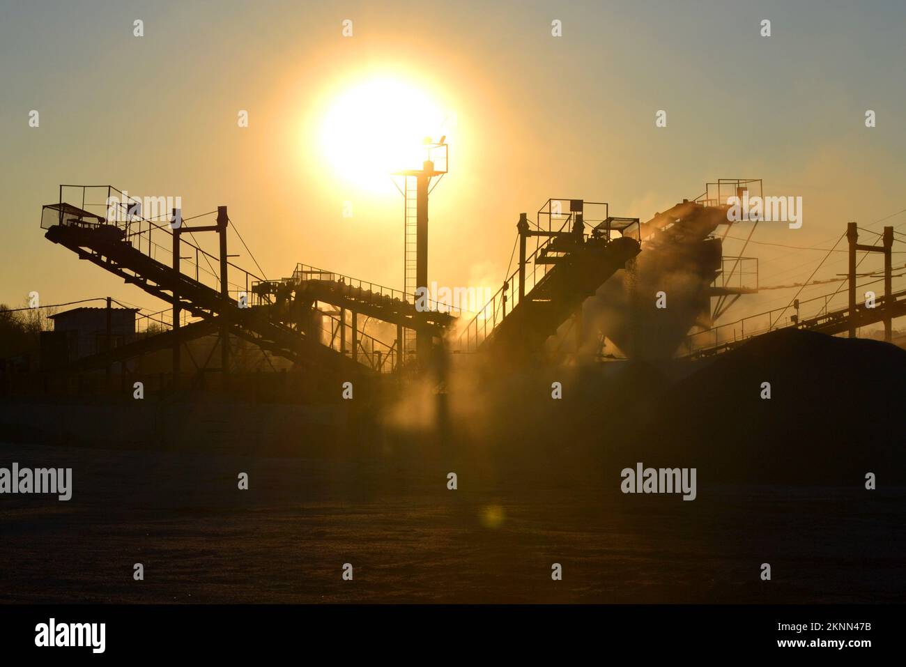 Cava mineraria. Impianto di frantumazione in cava di granito all'alba del tramonto. Frantumatore in cava. Molta polvere. Schiacciamento della pietra. Produzione industriale di ghiaia. Convogliatore ghiaia. Frantumatore a cono, sole splendente Foto Stock