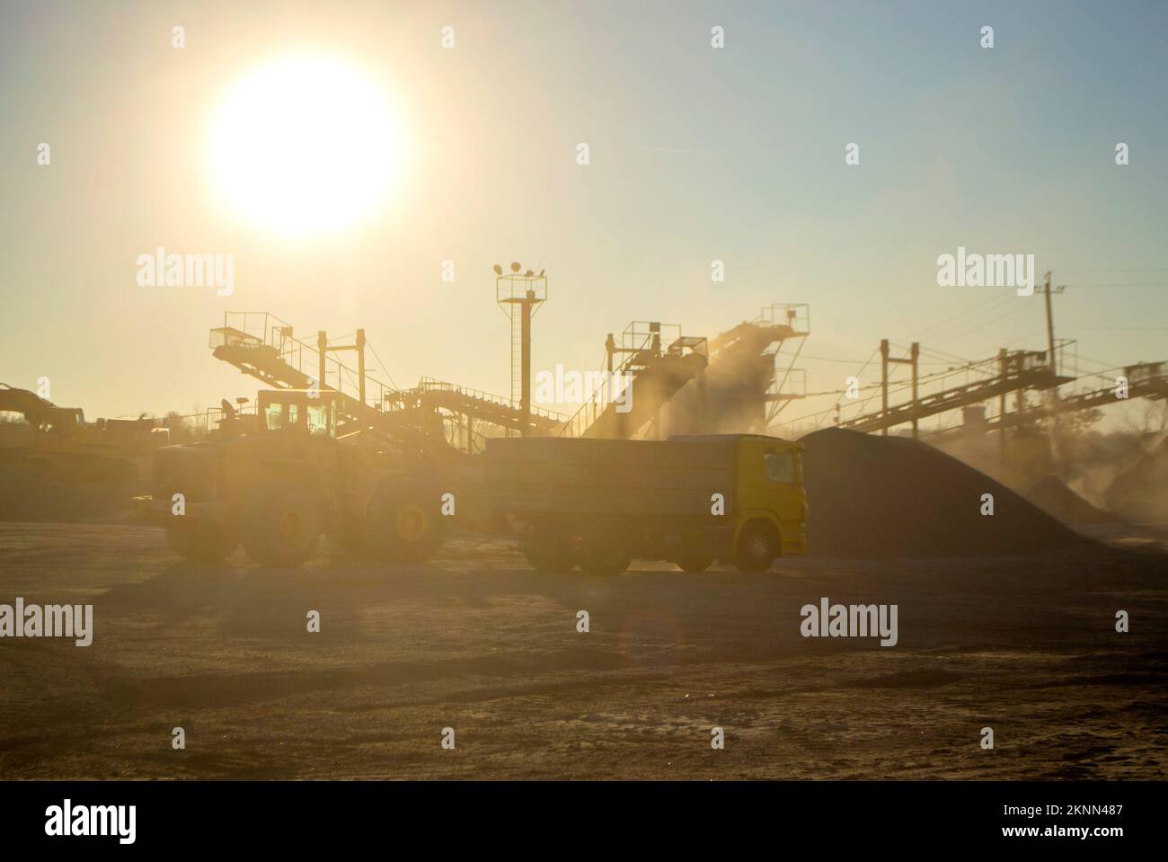 Cava mineraria. Impianto di frantumazione in cava di granito all'alba del tramonto. Frantumatore in cava. Molta polvere. Schiacciamento della pietra. Produzione industriale di ghiaia. Convogliatore ghiaia. Frantumatore a cono, sole splendente Foto Stock