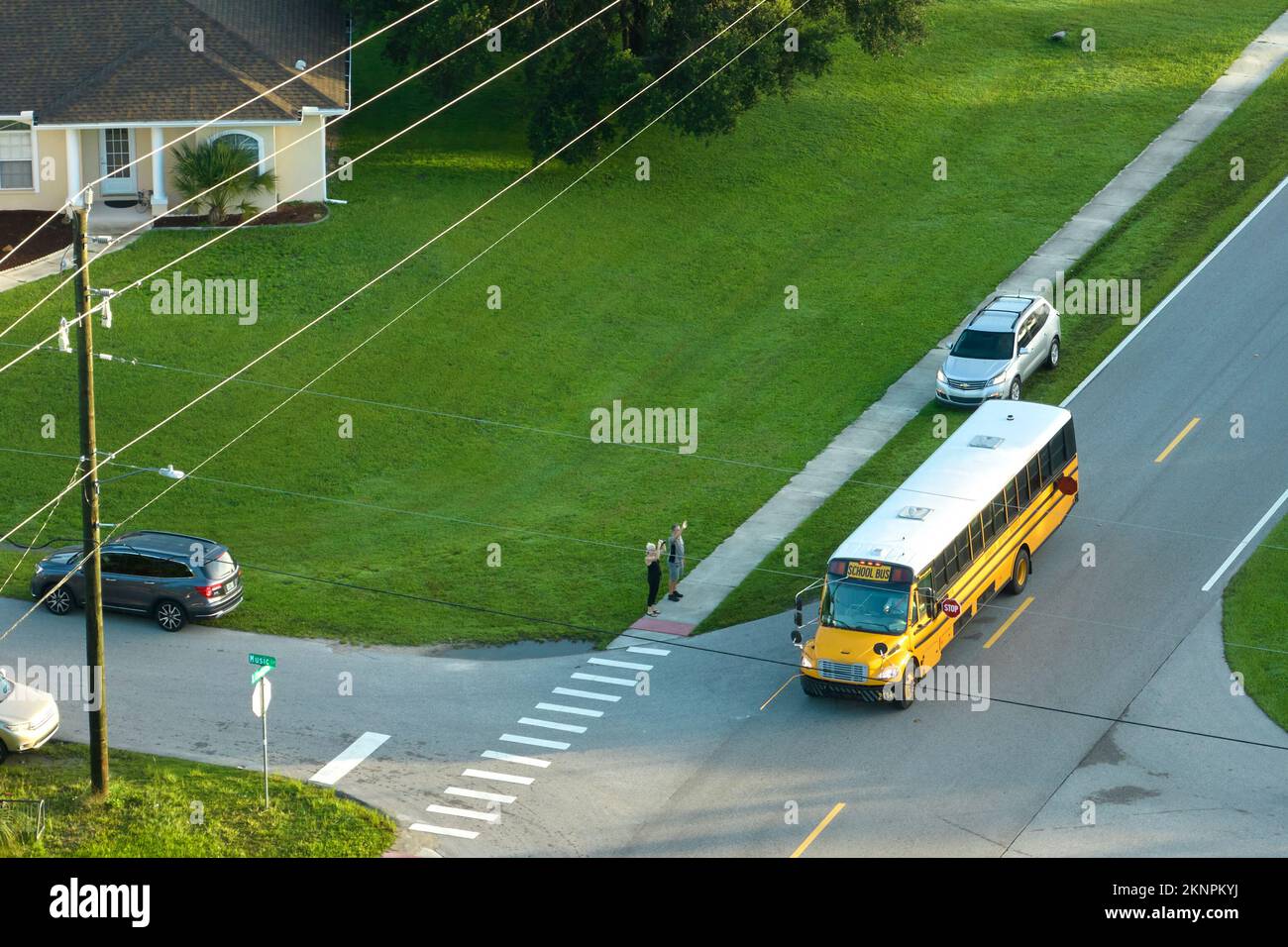 Veduta aerea dell'autobus americano giallo scuola che raccoglie i bambini alla fermata dell'autobus marciapiede per i loro lessong in prima mattina. Trasporto pubblico nel Foto Stock