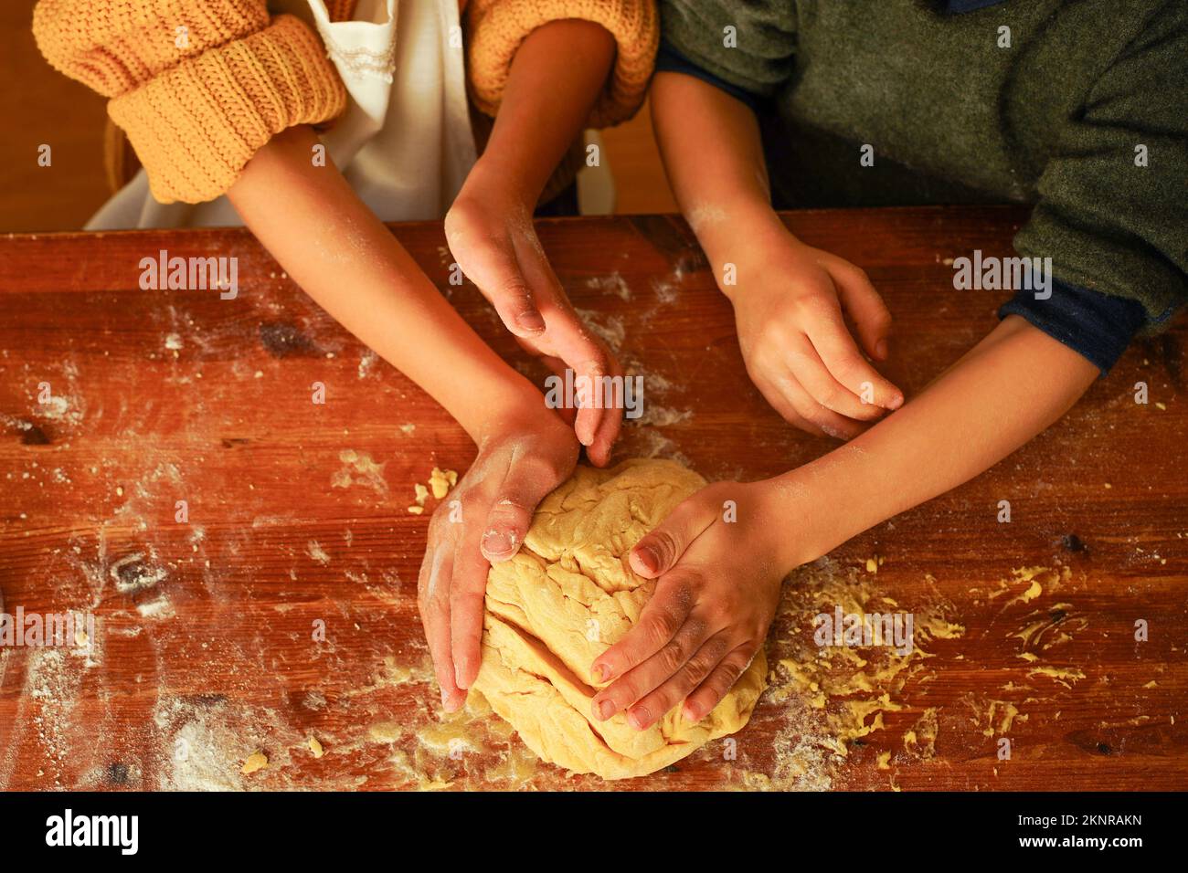 Mani dei bambini che impastano l'impasto dei biscotti con le mani su un tavolo di legno. Foto Stock