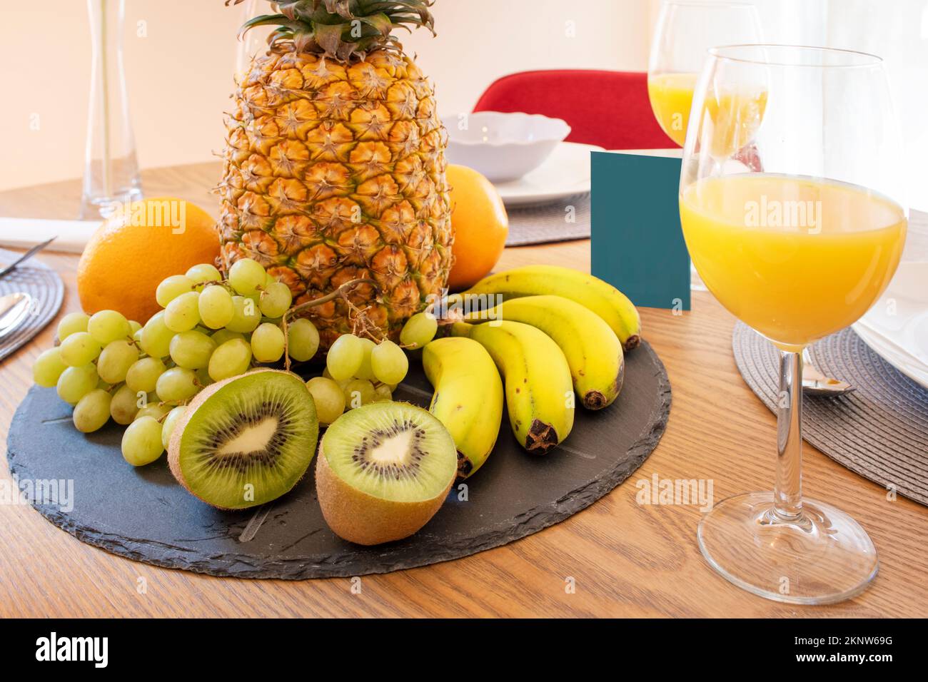 Un tavolo in legno di quercia con un pezzo centrale di ananas, banane mature, kiwi spaccati, uva bianca e agrumi Foto Stock