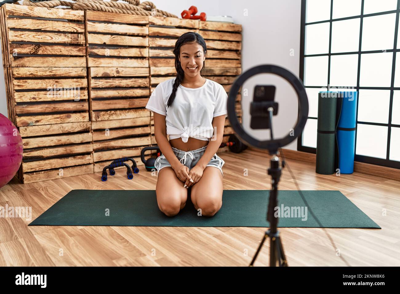 Giovane donna ispanica registrazione tutorial di allenamento in palestra guardando positivo e felice in piedi e sorridente con un sorriso fiducioso mostrando i denti Foto Stock