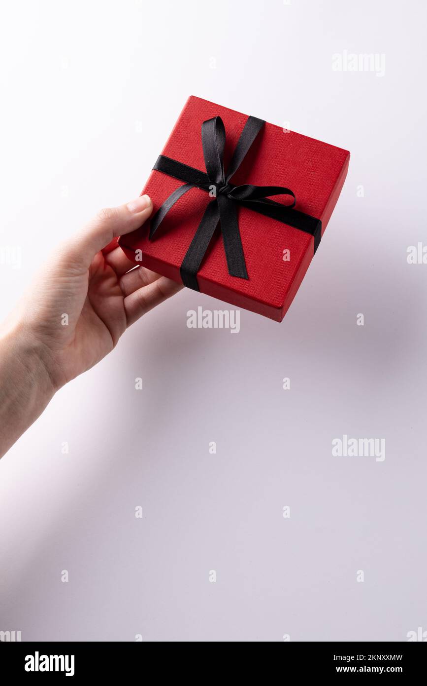 Verticale di mano che dà scatola regalo rossa legata con nastro nero, su sfondo bianco con spazio copia Foto Stock